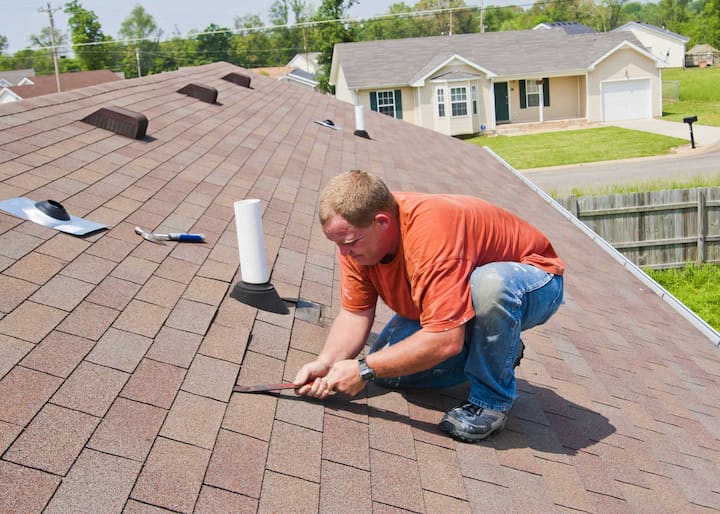 Wearing blue work boots a roofing repair expert works on Lithia Springs, Georgia home